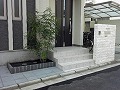 白い長方形自然石タイルを門柱に貼り付け、グレー色のピンコロで花壇を造り、植栽を植えた外構工事の施工画像