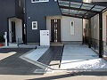 アプローチは建物のグレー色と同色系の自然石タイルを使用/門柱は高級感ある白い天然石を貼り付けた画像
