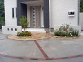 建物の玄関前に背の低い塀を2ヶ所に建て、その周りはサークル状に天然石とレンガでアートにしました/更にその周りはコンクリート打ちをした外構工事の施工画像